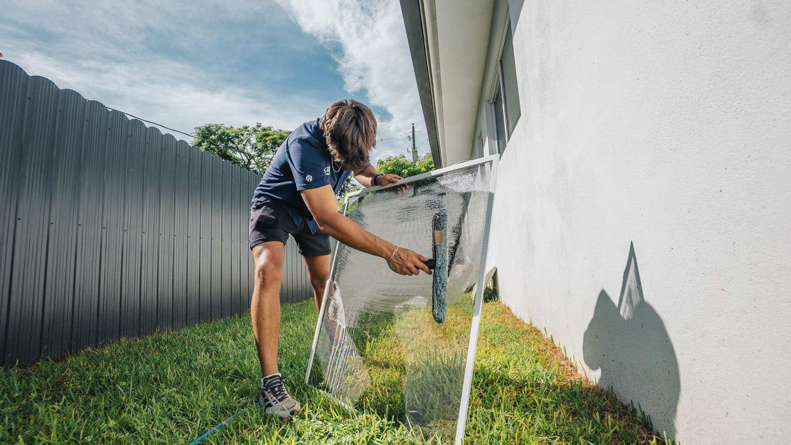 Coast technician washing a removed window screen with a soft brush at a Miami home