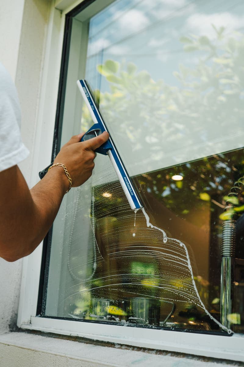 Hand squeegee pulling water off a ground-floor window pane on a Miami home